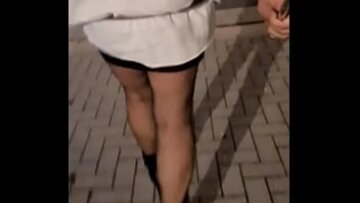 O travestită curvă în ciorapi și tocuri înalte se plimbă pe o parcare, arătându-și fundul mare și fundul cu bule